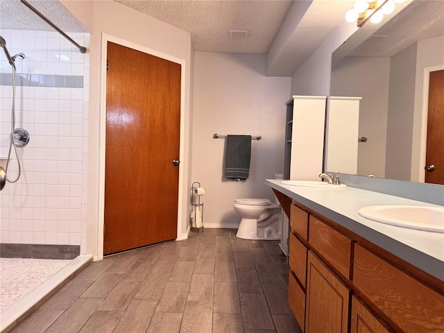 full bath featuring a textured ceiling, toilet, wood finished floors, a sink, and tiled shower