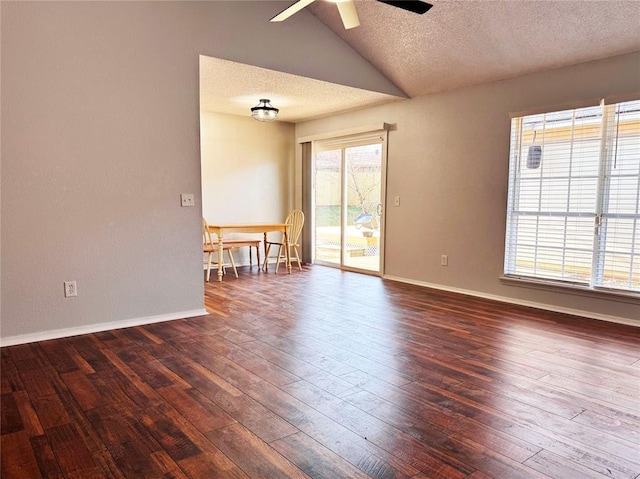 spare room with dark wood-style floors, vaulted ceiling, a textured ceiling, and baseboards