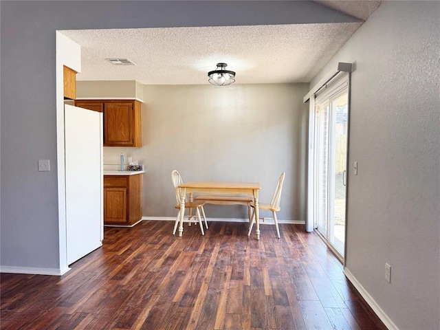 unfurnished dining area featuring dark wood-style floors, baseboards, visible vents, and a textured ceiling