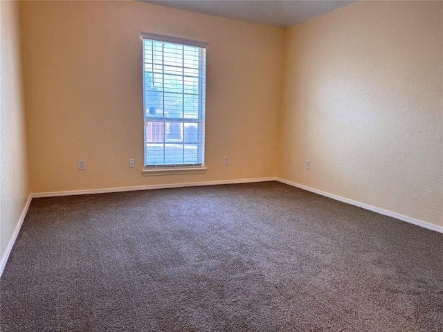 unfurnished room featuring baseboards and dark colored carpet