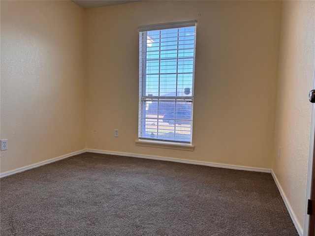 spare room featuring baseboards and dark carpet