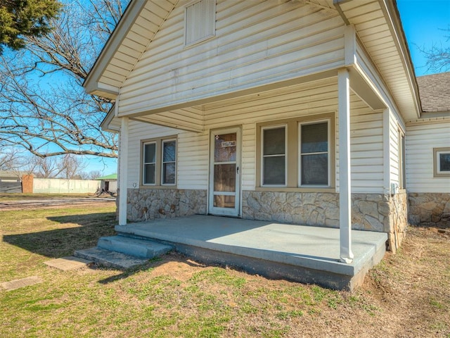 doorway to property featuring stone siding, a lawn, and roof with shingles