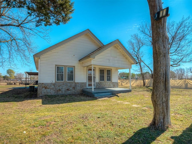 back of house featuring central air condition unit, stone siding, covered porch, and a yard