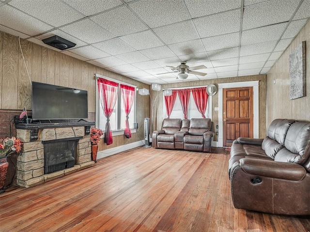 living room featuring a stone fireplace, a paneled ceiling, hardwood / wood-style flooring, and a ceiling fan