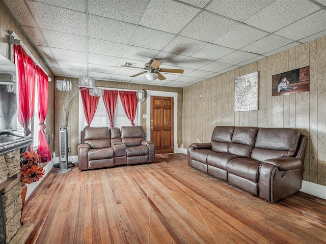 living area featuring baseboards, a drop ceiling, ceiling fan, wood finished floors, and wood walls