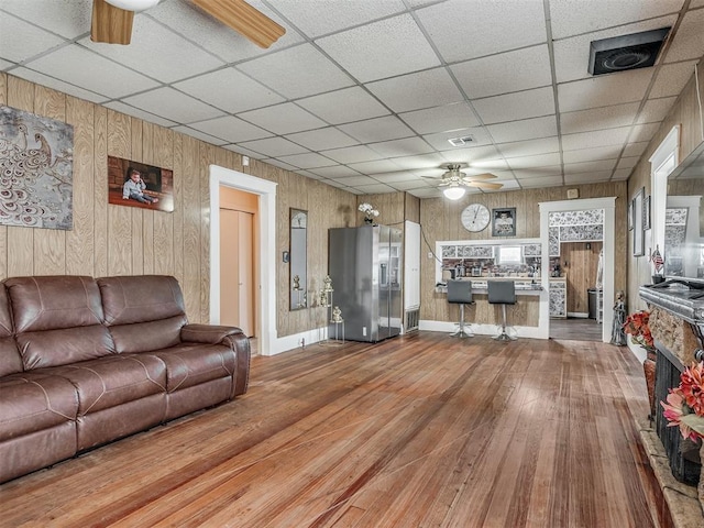 living area with wood walls, a drop ceiling, wood finished floors, and a ceiling fan