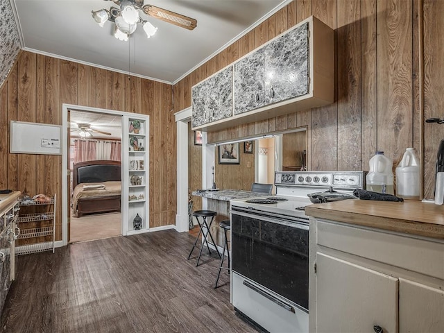 kitchen featuring white range with electric stovetop, dark wood finished floors, ceiling fan, crown molding, and wood walls