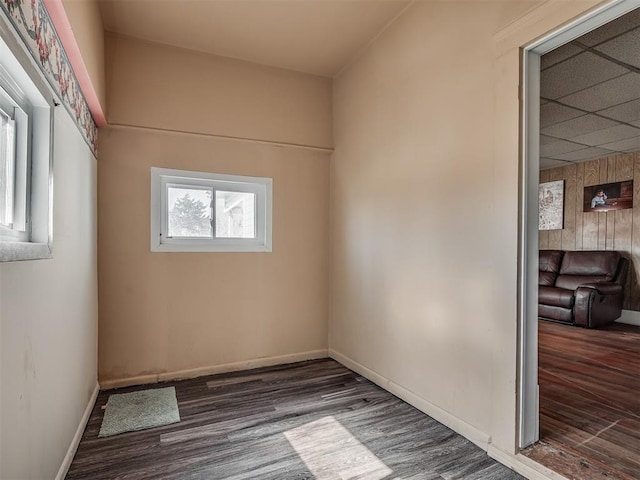 spare room with a drop ceiling, wood walls, baseboards, and wood finished floors