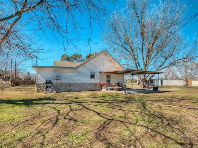 view of side of home featuring a carport, a yard, stone siding, and fence