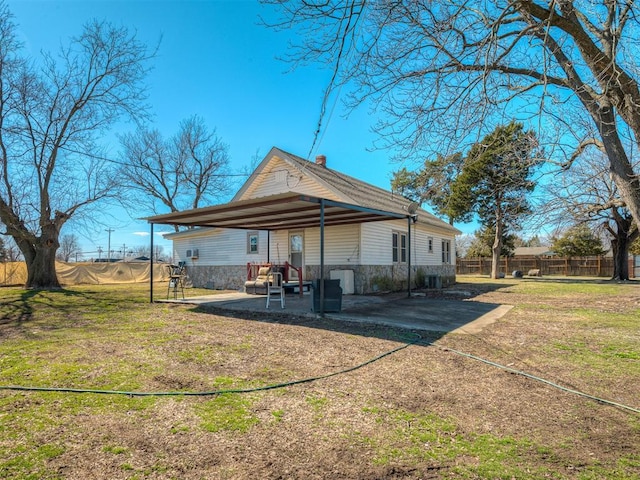 rear view of house featuring a yard, stone siding, a patio area, and fence