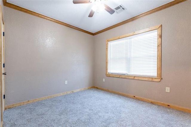 carpeted spare room featuring ceiling fan, baseboards, visible vents, and crown molding