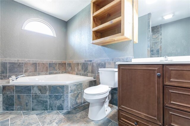 bathroom with toilet, a garden tub, a textured wall, and vanity