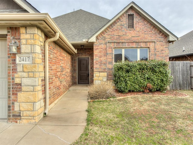 doorway to property with brick siding, roof with shingles, fence, a garage, and stone siding