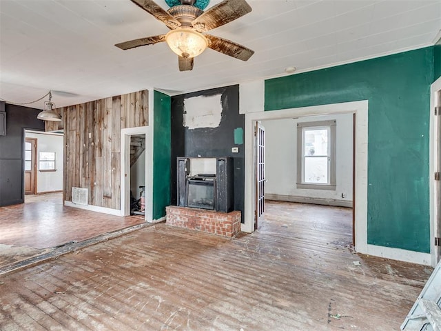 unfurnished living room with wooden walls, a ceiling fan, visible vents, a brick fireplace, and hardwood / wood-style floors