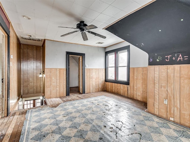 empty room with a wainscoted wall, visible vents, hardwood / wood-style flooring, and wooden walls