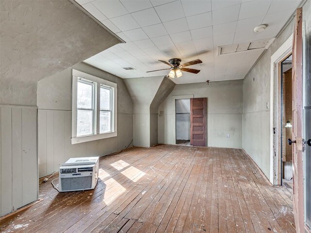 additional living space featuring a wall unit AC, a wainscoted wall, wood-type flooring, visible vents, and a ceiling fan