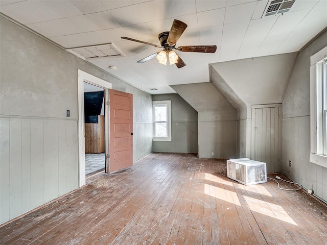 additional living space with wooden walls, visible vents, a wainscoted wall, wood-type flooring, and ceiling fan