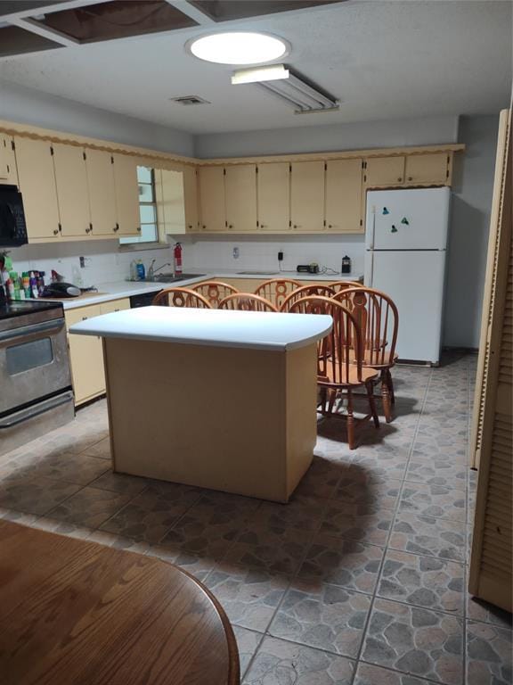 kitchen featuring black microwave, range with electric stovetop, light countertops, cream cabinetry, and freestanding refrigerator