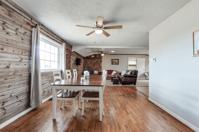 dining room with baseboards, a ceiling fan, lofted ceiling, wood-type flooring, and a textured ceiling