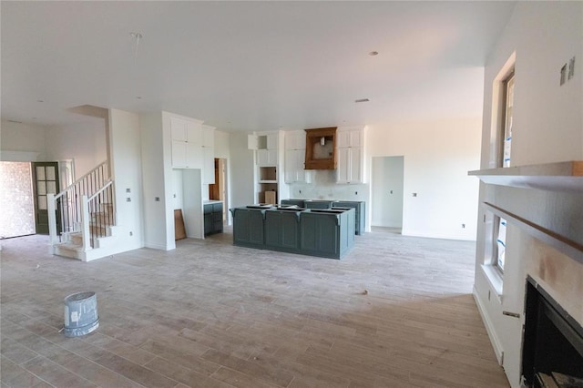 kitchen featuring white cabinets, open floor plan, baseboards, light wood-style floors, and a fireplace