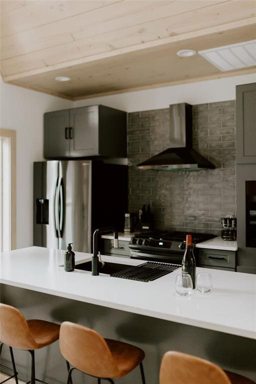 kitchen featuring a breakfast bar, decorative backsplash, appliances with stainless steel finishes, wood ceiling, and wall chimney exhaust hood