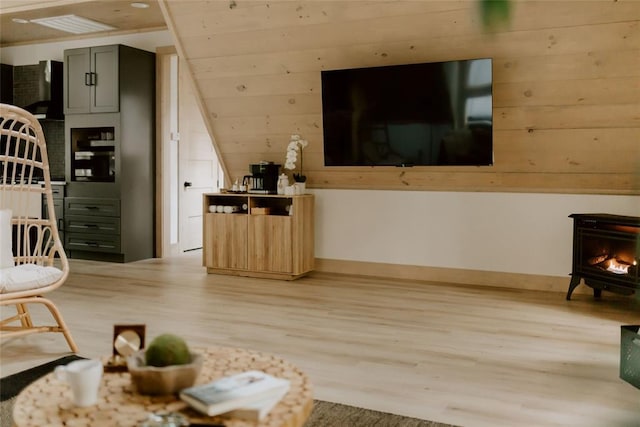 living room with vaulted ceiling, light wood finished floors, a wood stove, and baseboards