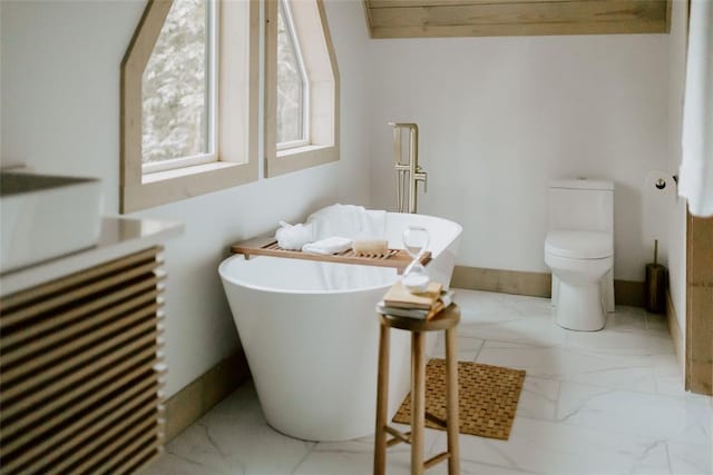 full bath with toilet, marble finish floor, and a freestanding tub