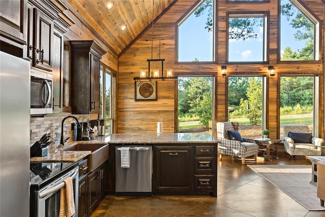 kitchen with wooden walls, appliances with stainless steel finishes, light stone countertops, high vaulted ceiling, and a sink