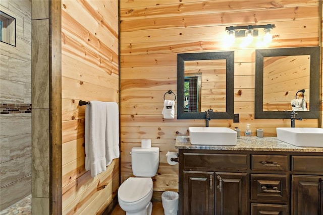 bathroom with toilet, double vanity, wooden walls, and a sink