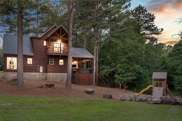 exterior space featuring a playground, a lawn, metal roof, a balcony, and log veneer siding