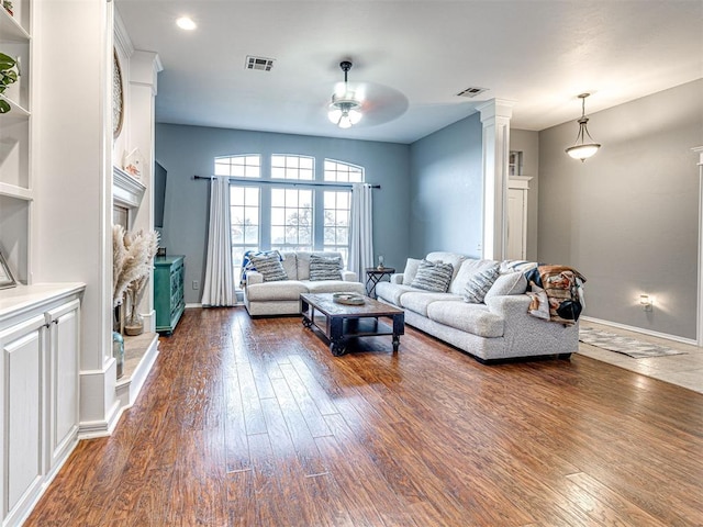 living room featuring dark wood-style flooring, decorative columns, and visible vents