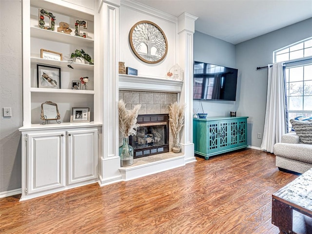 living area featuring built in shelves, a fireplace, baseboards, and wood finished floors