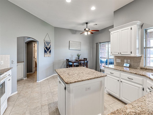 kitchen with arched walkways, a center island, electric stove, tasteful backsplash, and white cabinets