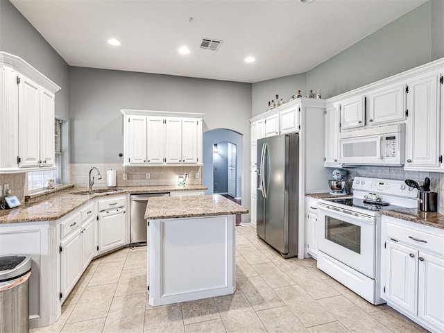 kitchen featuring arched walkways, light stone counters, stainless steel appliances, a sink, and white cabinets