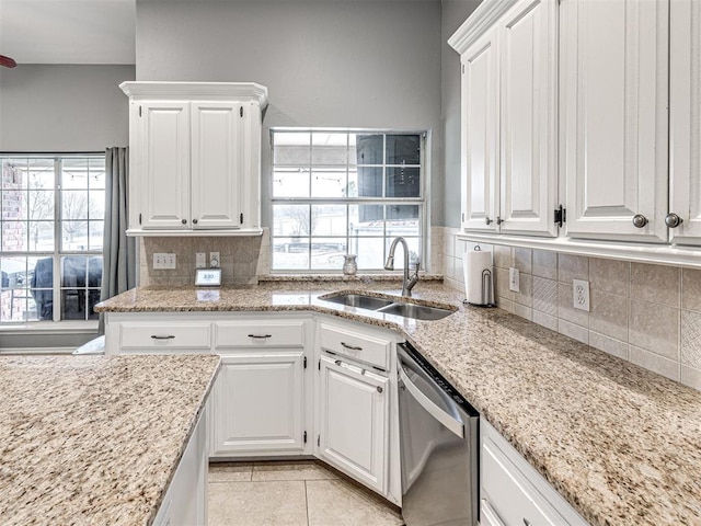 kitchen with light tile patterned floors, tasteful backsplash, stainless steel dishwasher, white cabinetry, and a sink