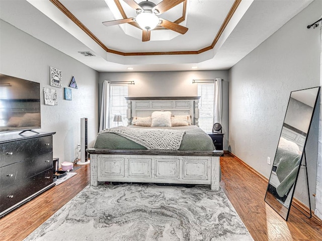 bedroom featuring a tray ceiling, visible vents, crown molding, and light wood finished floors