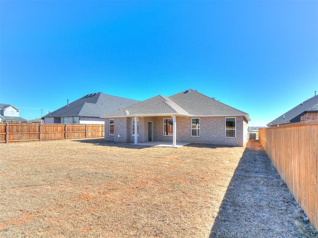 rear view of property with a fenced backyard, brick siding, a shingled roof, a lawn, and a patio area