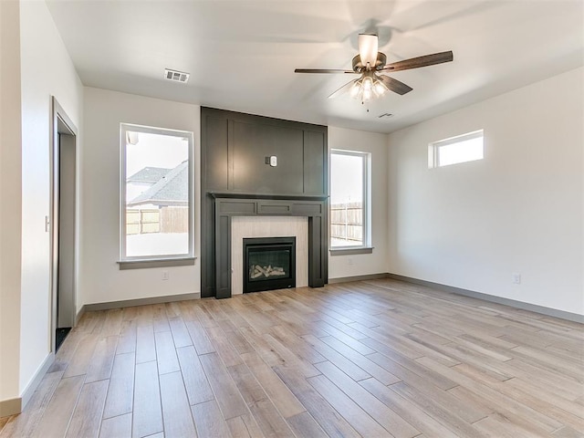 unfurnished living room featuring light wood finished floors, baseboards, visible vents, a ceiling fan, and a fireplace