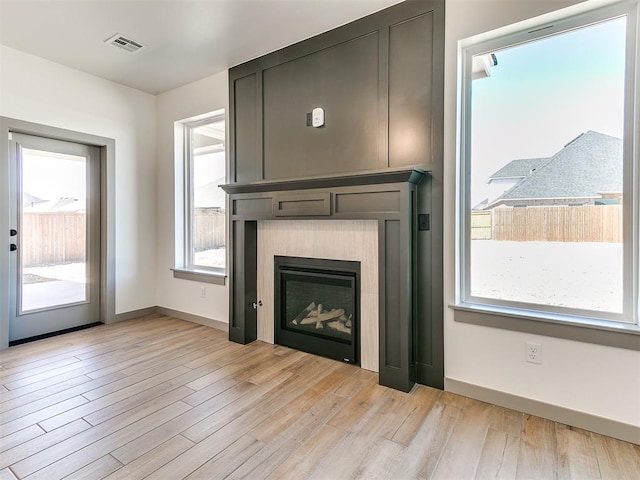 unfurnished living room featuring a large fireplace, baseboards, visible vents, and light wood-style floors