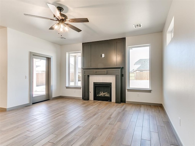 unfurnished living room featuring light wood finished floors, visible vents, a ceiling fan, a large fireplace, and baseboards