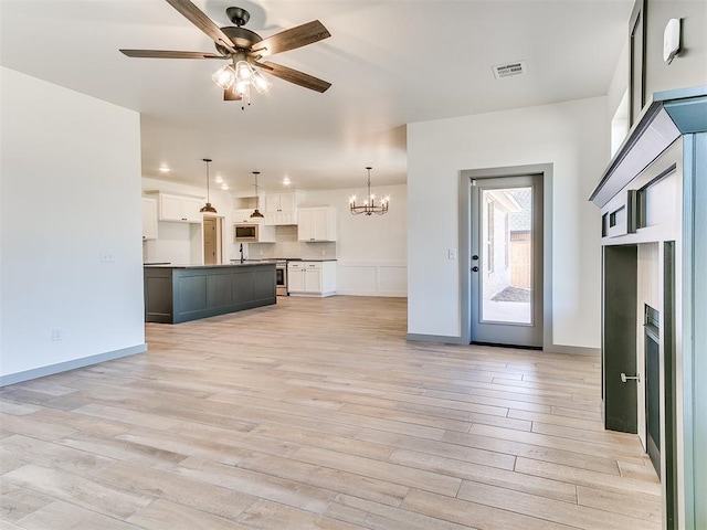 unfurnished living room featuring light wood-type flooring, visible vents, baseboards, and ceiling fan with notable chandelier