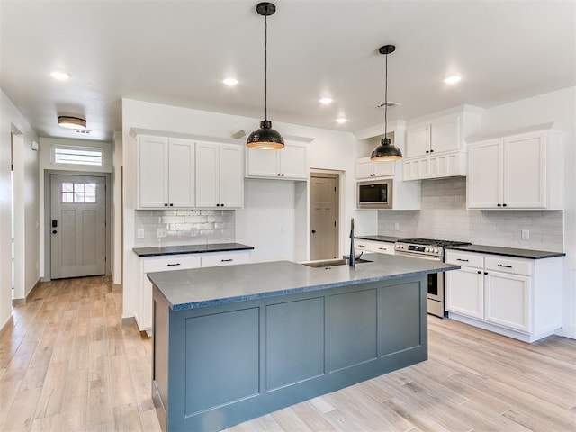 kitchen featuring light wood finished floors, dark countertops, appliances with stainless steel finishes, white cabinetry, and a sink