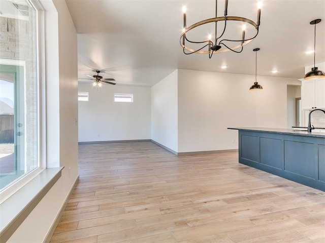 kitchen featuring baseboards, white cabinets, light wood-type flooring, a sink, and ceiling fan with notable chandelier