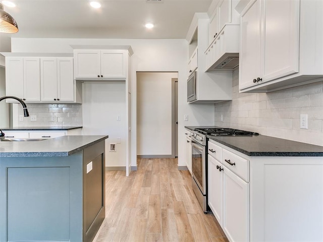 kitchen with a sink, white cabinets, light wood-style floors, appliances with stainless steel finishes, and dark countertops