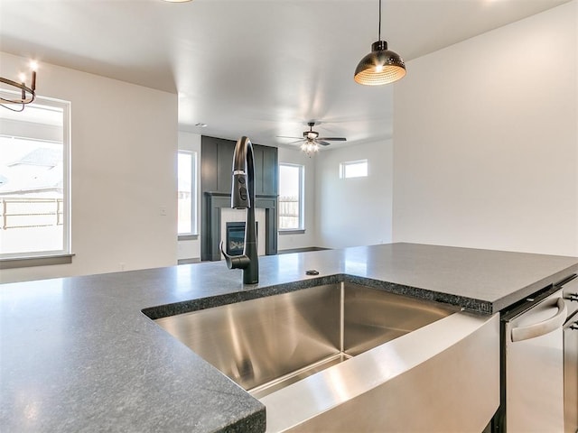 kitchen featuring pendant lighting, a fireplace, dark countertops, a sink, and ceiling fan