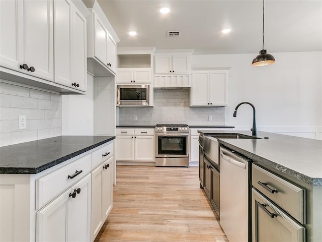 kitchen featuring dark countertops, visible vents, appliances with stainless steel finishes, light wood-style floors, and a sink