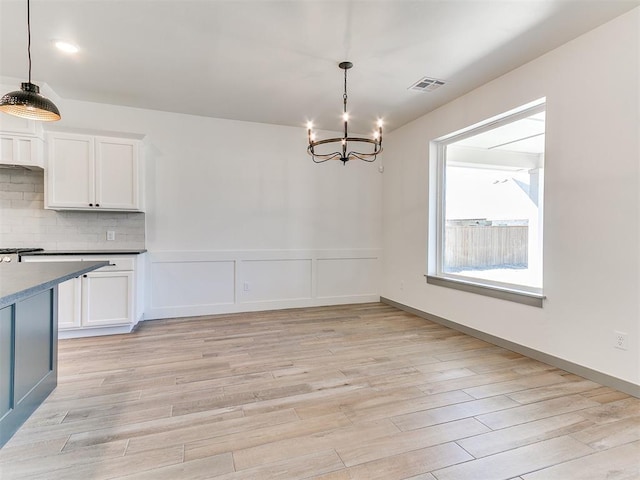 unfurnished dining area with a wainscoted wall, a notable chandelier, visible vents, a decorative wall, and light wood-type flooring