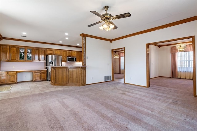 unfurnished living room with baseboards, visible vents, light colored carpet, ornamental molding, and built in desk