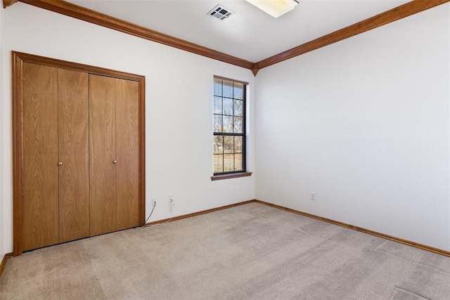 unfurnished bedroom with carpet flooring, visible vents, baseboards, ornamental molding, and a closet