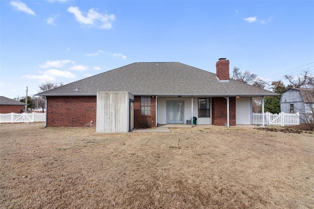 rear view of house featuring brick siding, a chimney, a shingled roof, a lawn, and fence